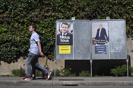 Des piétons passent devant des affiches de campagne du président français et candidat du parti La République en Marche (LREM), Emmanuel Macron, et de la candidate du Rassemblement National (RN), Marine Le Pen, à Eguisheim, dans l'est de la France, le 21 avril 2022, à la veille du second tour de l'élection présidentielle.