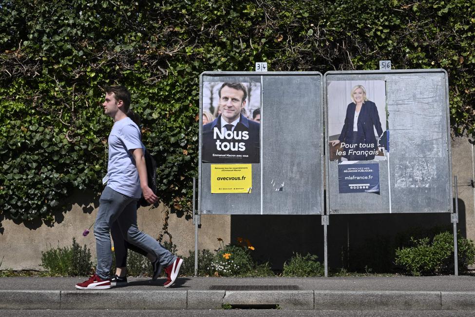 Des piétons passent devant des affiches de campagne du président français et candidat du parti La République en Marche (LREM), Emmanuel Macron, et de la candidate du Rassemblement National (RN), Marine Le Pen, à Eguisheim, dans l'est de la France, le 21 avril 2022, à la veille du second tour de l'élection présidentielle.