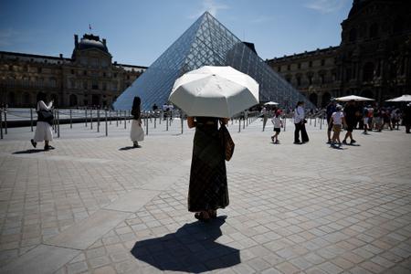 Une personne se protège du soleil sous un parasol devant le musée du Louvre à Paris, alors qu'une vague de chaleur précoce et record frappe une grande partie de l'Europe occidentale, le 28 mai 2026.