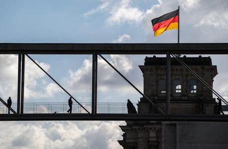 Des personnes traversent un pont piétonnier alors qu'un drapeau allemand flotte sur le bâtiment du Reichstag à Berlin, le 23 octobre 2024.