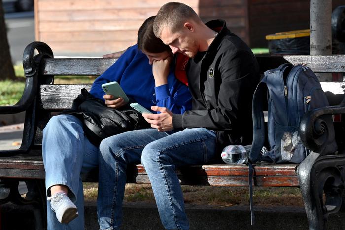 Un couple regarde leurs téléphones portables alors qu'ils sont assis sur un banc au centre de la ville ukrainienne de Kiev, par une chaude journée d'automne, le 3 octobre 2023.