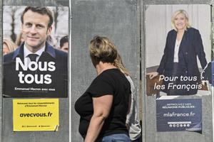 Des piétons passent devant des affiches de campagne du président français et candidat du parti La République en Marche (LREM), Emmanuel Macron, et de la candidate du Rassemblement National (RN), Marine Le Pen, à Eguisheim, dans l'est de la France, le 21 avril 2022, à la veille du second tour de l'élection présidentielle.
