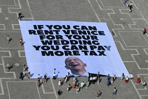 Une bannière anti-Bezos déployée sur la Place Saint Marc de Venise le 24 juin 2025, protestant contre le mariage du milliardaire dans la ville, dénonçant l'optimisation fiscale et le coût environnemental et social de l'événement. (Photo by Stefano Rellandini / AFP)