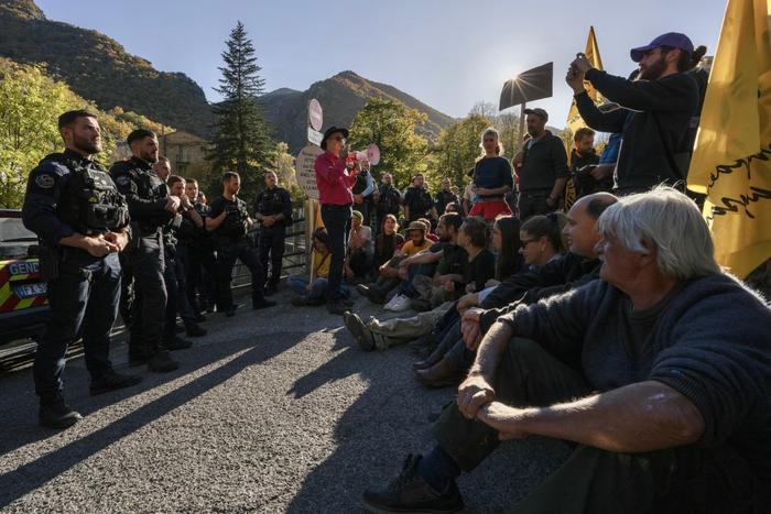 Des manifestants, assis sur la chaussée face à des gendarmes français, protestent contre l'abattage d'environ 80 bovins atteints de dermatose bovine à Thues-Entre-Valls, dans le sud-ouest de la France, le 3 novembre 2025.