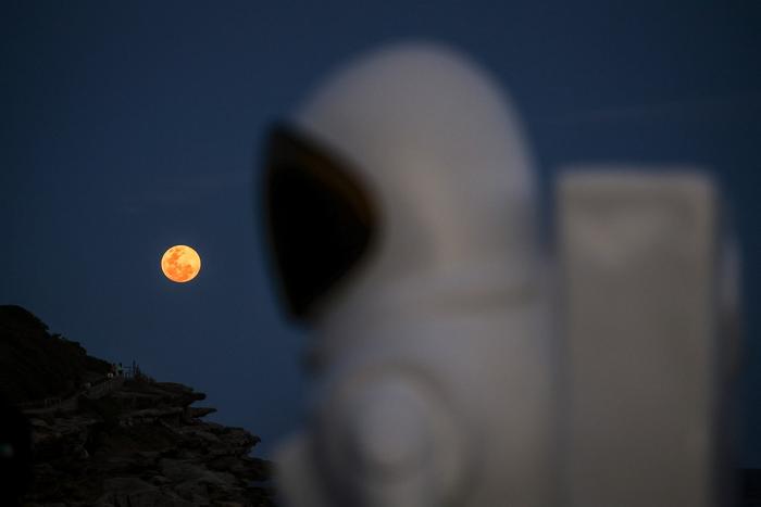 Une super lune se lève derrière une sculpture d'astronaute faisant partie de l'exposition Sculpture by the Sea, sur un promontoire à Sydney, le 17 octobre 2024.