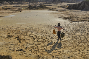Un homme transporte de l'eau à travers un paysage aride à Sagaing, révélant l'impact de la sécheresse.