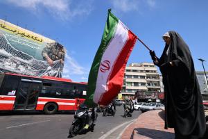 Une femme agite le drapeau national iranien devant un panneau d'affichage géant indiquant « Le détroit d'Ormuz reste fermé » sur la place de la Révolution à Téhéran, le 12 avril 2026.
