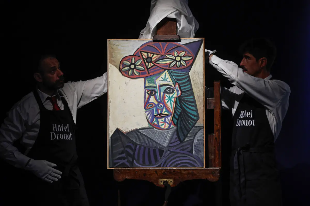 Des employés dévoilent un tableau de l'artiste espagnol Pablo Picasso intitulé « Buste de femme au chapeau fleuri » et représentant l'une de ses amantes, Dora Maar, lors de sa présentation à l'hôtel Drouot, le 18 septembre 2025. (Photo : Stéphane de Sakutin / AFP)