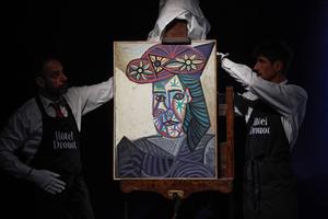 Des employés dévoilent un tableau de l'artiste espagnol Pablo Picasso intitulé « Buste de femme au chapeau fleuri » et représentant l'une de ses amantes, Dora Maar, lors de sa présentation à l'hôtel Drouot, le 18 septembre 2025. (Photo : Stéphane de Sakutin / AFP)