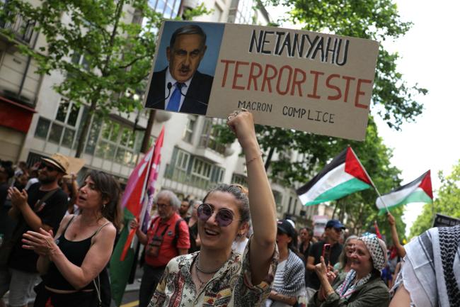 Une jeune manifestante tient une pancarte représentant le Premier ministre israélien Benjamin Netanyahu grimé d'une moustache rappelant celle d'Adolf Hitler, lors d'une manifestation pro-palestinienne à Paris, le 14 juin 2025.