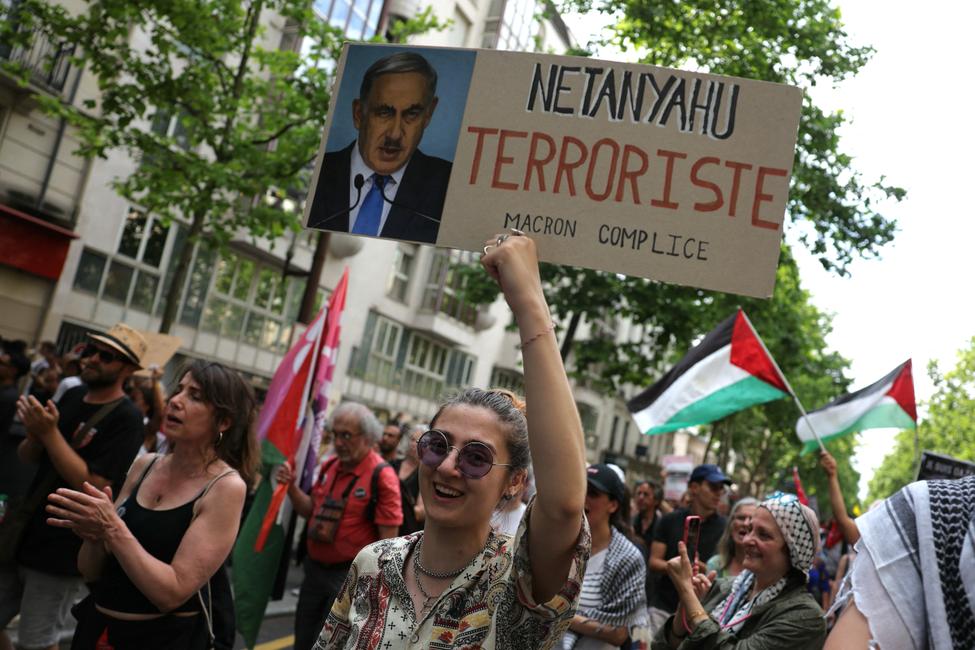 Une jeune manifestante tient une pancarte représentant le Premier ministre israélien Benjamin Netanyahu grimé d'une moustache rappelant celle d'Adolf Hitler, lors d'une manifestation pro-palestinienne à Paris, le 14 juin 2025.