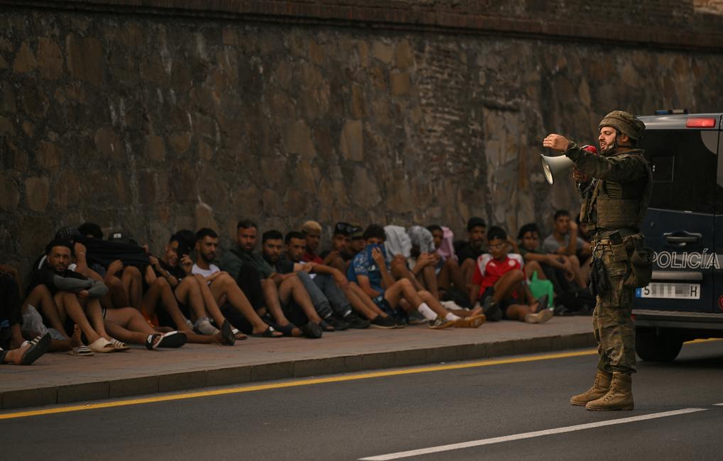 Un soldat espagnol utilise un mégaphone pour s'adresser à des migrants assis sur le trottoir avant de les escorter vers le Maroc, dans l'enclave espagnole de Ceuta, en Afrique du Nord, le 1er août 2026. Au moins 67 personnes ont trouvé la mort lors de la récente vague de traversées migratoires entre le Maroc et l'enclave espagnole de Ceuta, a annoncé ce jour-là le ministre espagnol de l'Intérieur. La plupart des quelque 60 000 migrants entrés à Ceuta en l'espace de quelques jours depuis le Maroc voisin sont déjà retournés au Maroc. (Image d'illustration)