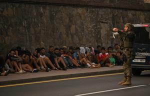 Un soldat espagnol utilise un mégaphone pour s'adresser à des migrants assis sur le trottoir avant de les escorter vers le Maroc, dans l'enclave espagnole de Ceuta, en Afrique du Nord, le 1er août 2026. Au moins 67 personnes ont trouvé la mort lors de la récente vague de traversées migratoires entre le Maroc et l'enclave espagnole de Ceuta, a annoncé ce jour-là le ministre espagnol de l'Intérieur. La plupart des quelque 60 000 migrants entrés à Ceuta en l'espace de quelques jours depuis le Maroc voisin sont déjà retournés au Maroc. (Image d'illustration)