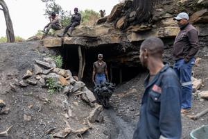 Un mineur pousse une brouette remplie de charbon hors de la mine de Golfview, à Ermelo, en Afrique du Sud, tandis que d'autres personnes se tiennent à l'entrée.