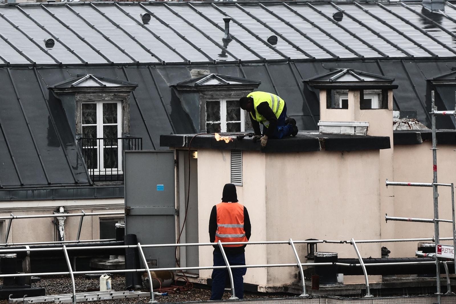 Des ouvriers refont l'isolation bitumineuse du toit d'un immeuble à Paris.
