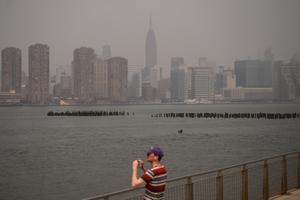 Un homme photographie Manhattan, enveloppée d'un épais brouillard de fumée provenant des incendies de forêt canadiens, à New York, le 30 juin 2023. 