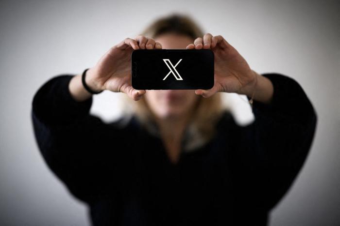 Une femme tient un smartphone arborant le logo du réseau social X.