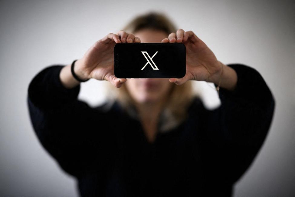 Une femme tient un smartphone arborant le logo du réseau social X.