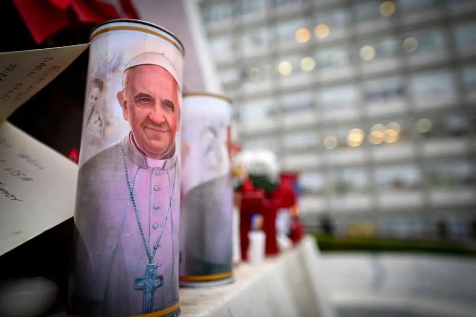 Une bougie avec un portrait du pape François est placée au pied d'une statue du pape Jean-Paul II à l'extérieur de l'hôpital Gemelli de Rome, le 19 février 2025.