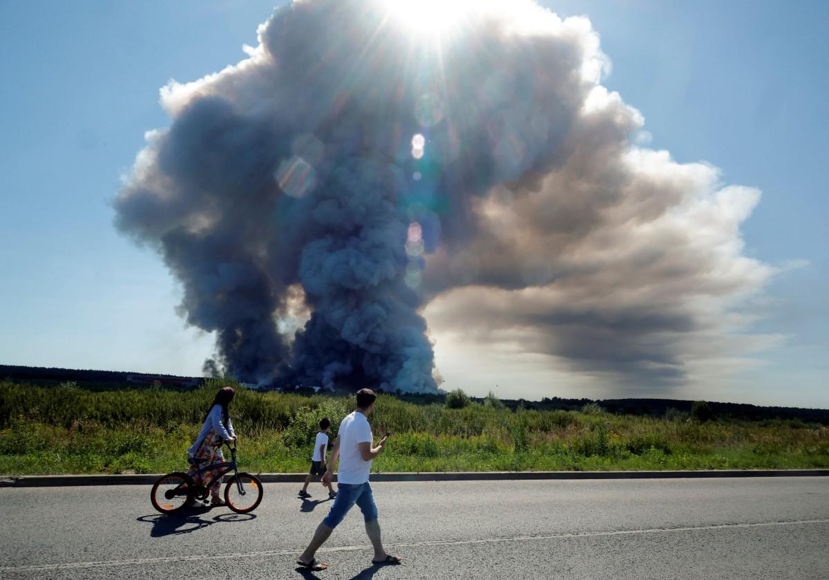 Des habitants passent devant la fumée d'un incendie survenu dans les complexes logistiques de l'entreprise russe de commerce en ligne Wildberries, à Elektrostal, près de Moscou, le 18 juillet 2026.