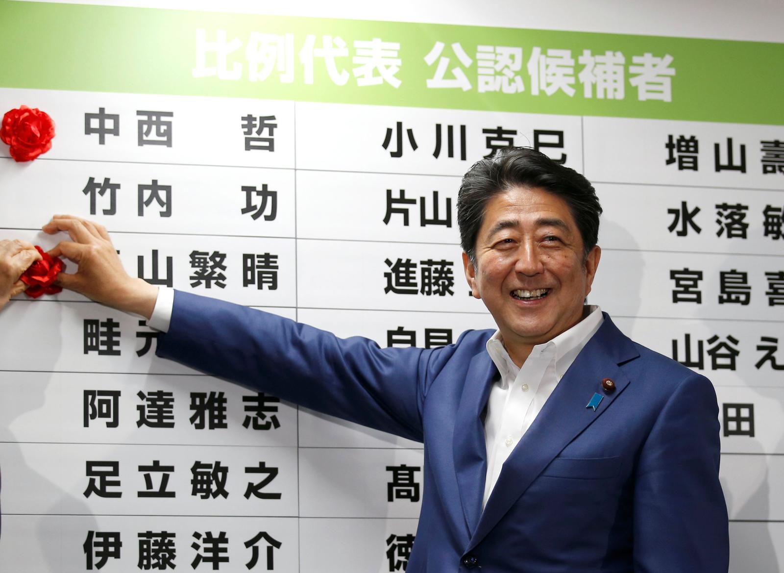 Le Premier ministre du Japon, Shinzo Abe, leader du Parti libéral démocrate (PLD), place une rosette sur le nom d'un candidat gagnant du PLD à l'élection de la Chambre haute, au siège du PLD à Tokyo, (Japon), le 10 juillet 2016.