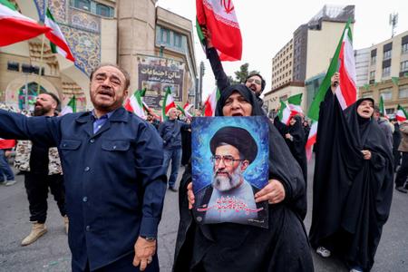 Une femme tient une illustration représentant le chef suprême iranien, l'ayatollah Ali Khamenei, tandis que d'autres agitent des drapeaux nationaux iraniens lors d'une manifestation de soutien au gouvernement à Téhéran, le 28 février 2026.