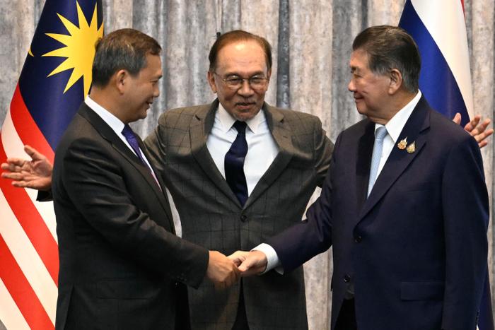Le Premier ministre cambodgien Hun Manet (à gauche) et le Premier ministre par intérim thaïlandais Phumtham Wechayachai (à droite) se serrent la main tandis que le Premier ministre malaisien Anwar Ibrahim (au centre) les entoure de ses bras à l’issue d’une conférence de presse, après des discussions sur un possible cessez-le-feu entre la Thaïlande et le Cambodge à Putrajaya, le 28 juillet 2025.