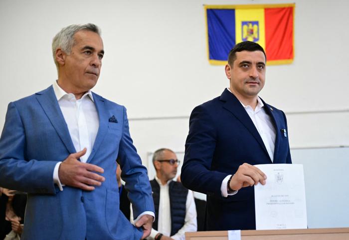 Le chef du parti nationaliste souverainiste « Alliance pour l'Union des Roumains » (AUR), George Simion, dépose son bulletin de vote aux côtés de l'ancien candidat Calin Georgescu lors du premier tour de l'élection présidentielle à Mogosoaia, le 4 mai 2025.