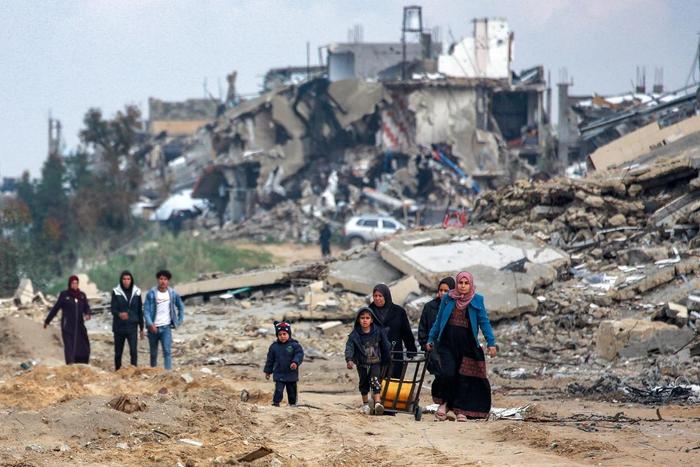Des femmes et des enfants marchent le long d'une route détruite devant des bâtiments effondrés, à l'ouest de Beit Lahia, dans le nord de la bande de Gaza, le 11 février 2025.