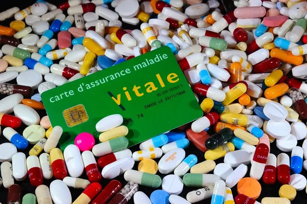Une Carte vitale, une carte d'assurance maladie à côté de gélules de médicaments et de pilules.