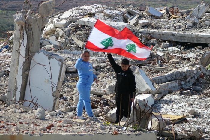 Des enfants libanais brandissent leur drapeau national en marchant au-dessus des décombres d'un bâtiment détruit, dans le sud du pays, le 28 janvier 2025.