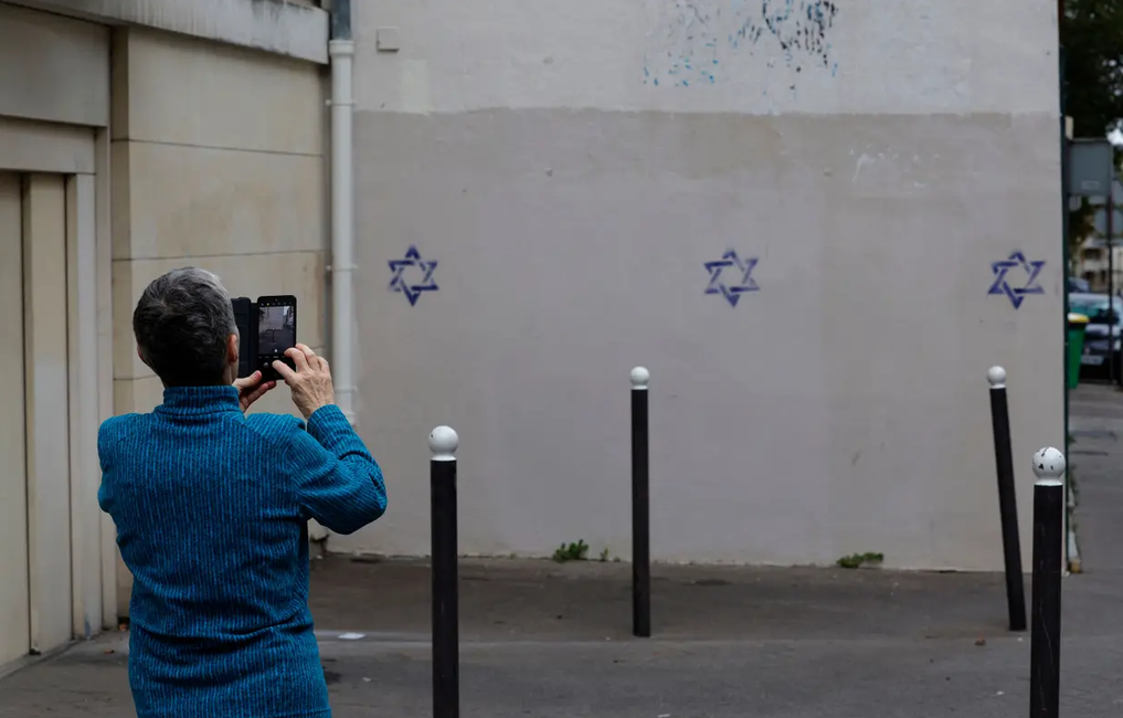 Une personne utilise un smartphone pour prendre des photos d'un mur d'immeuble recouvert d'étoiles de David peintes pendant la nuit, dans le quartier d'Alésia à Paris, le 31 octobre 2023.