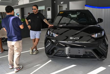 Un homme discute avec un vendeur à côté d'une voiture électrique BYD dans une concession automobile.