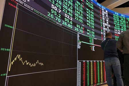 Des passants défilent devant un tableau affichant les cours des actions à la Bourse de Taïwan à Taipei, le 9 mars 2026.
