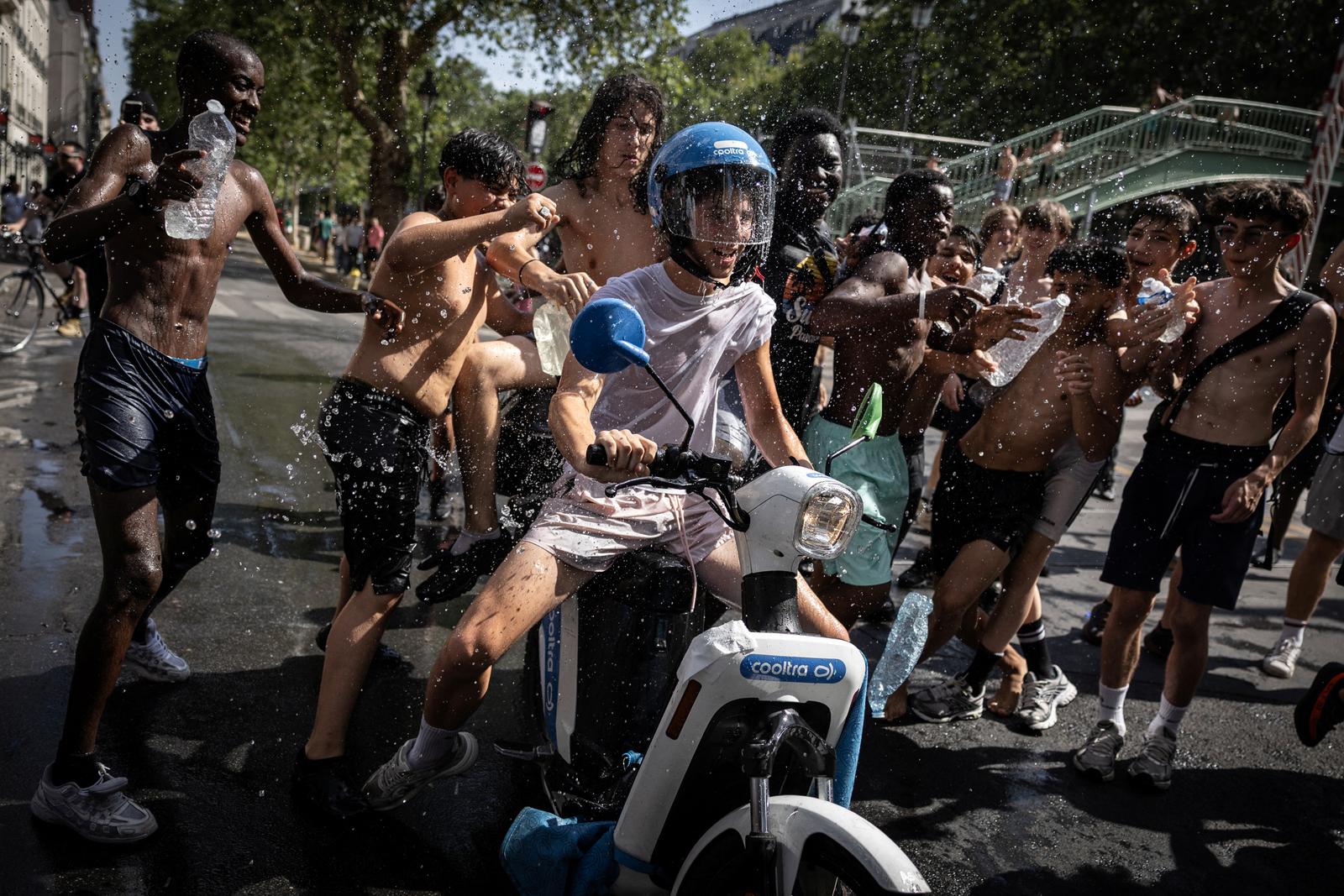 Un groupe d'adolescents jette de l'eau sur un jeune homme conduisant un scooter près du canal Saint-Martin, à Paris, le 24 juin 2026, en pleine vague de chaleur.