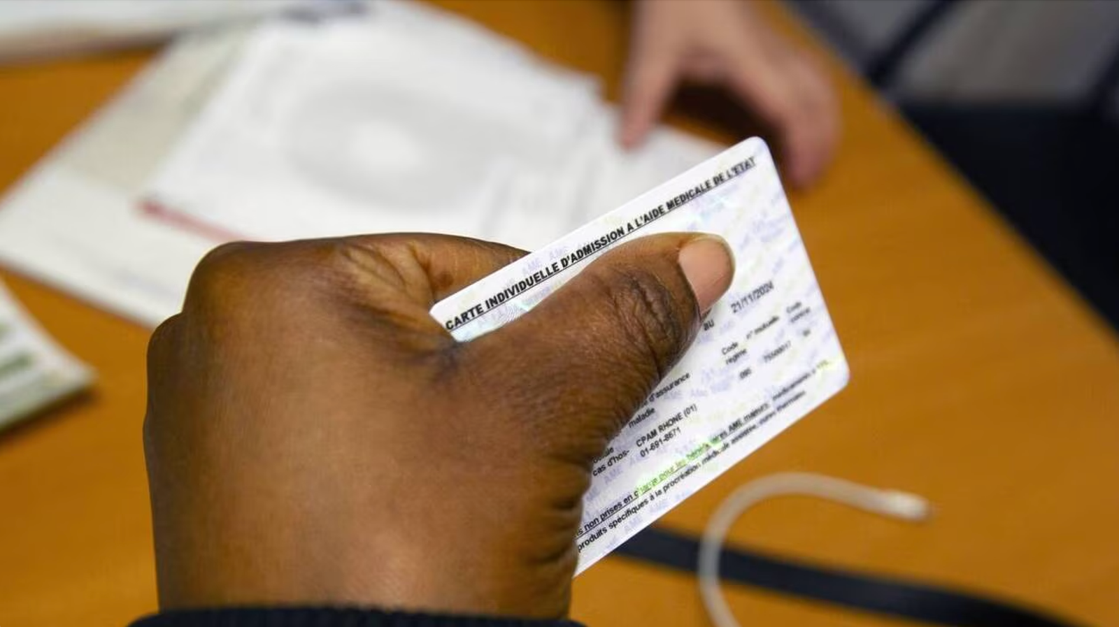 Une femme tient dans sa main sa carte d’affiliation à l’Aide médicale de l’État.