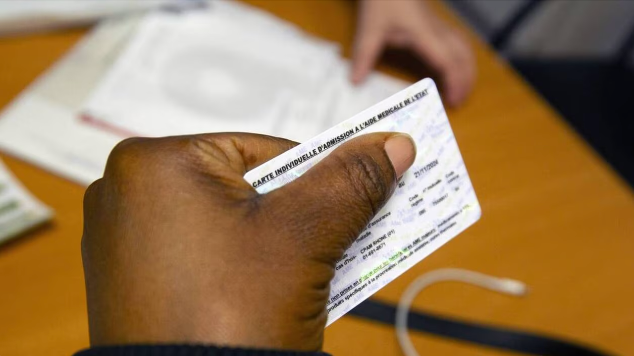 Une femme tient dans sa main sa carte d’affiliation à l’Aide médicale de l’État.