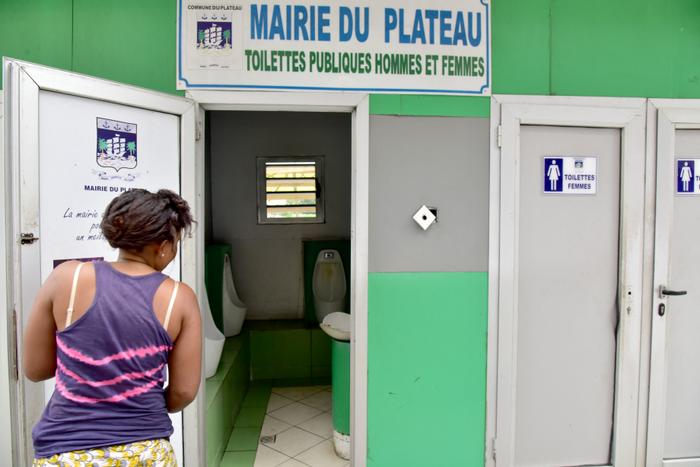Une femme regarde dans des toilettes publiques dans le quartier d'affaires du Plateau à Abidjan.