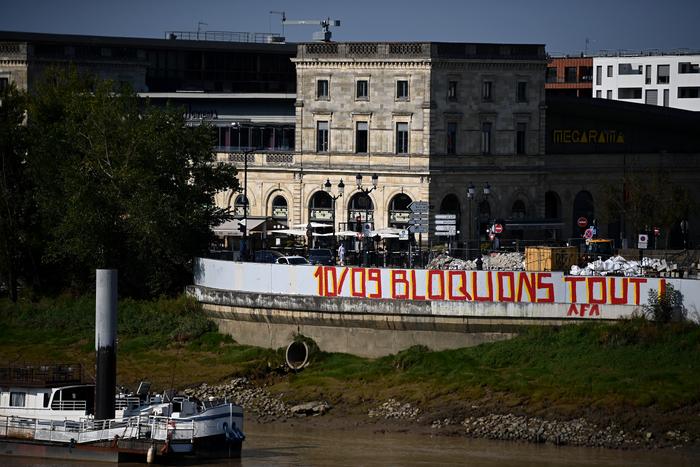 Le slogan du mouvement du 10 septembre, "Bloquons tout" inscrit sur un quais de la Garonne à Bordeaux en août 2025 (Photo de Christophe ARCHAMBAULT / AFP)