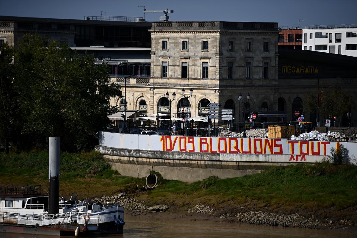 Le slogan du mouvement du 10 septembre, "Bloquons tout" inscrit sur un quais de la Garonne à Bordeaux en août 2025 (Photo de Christophe ARCHAMBAULT / AFP)
