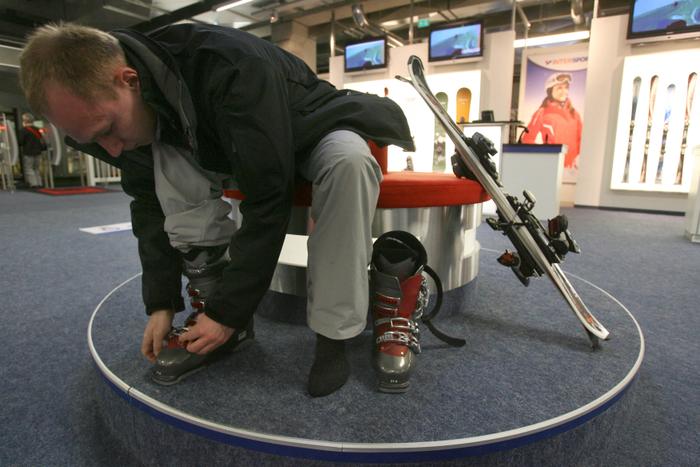 Un client enfile des chaussures de ski dans un magasin.