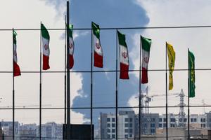 Des drapeaux iraniens à Téhéran, tandis qu'un panache de fumée s'élève d'une raffinerie de pétrole en arrière-plan, le 15 juin 2025.