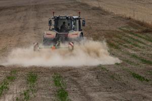 Un agriculteur conduit un tracteur équipé d'un râteau pour travailler la terre dans un champ à Condé-sur-Risle.