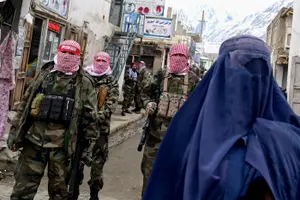 Des agents de sécurité talibans montent la garde tandis qu'une femme afghane vêtue d'une burqa marche dans la rue d'un marché du district de Baharak, dans la province du Badakhshan, le 26 février 2024. (Image d'illustration)
