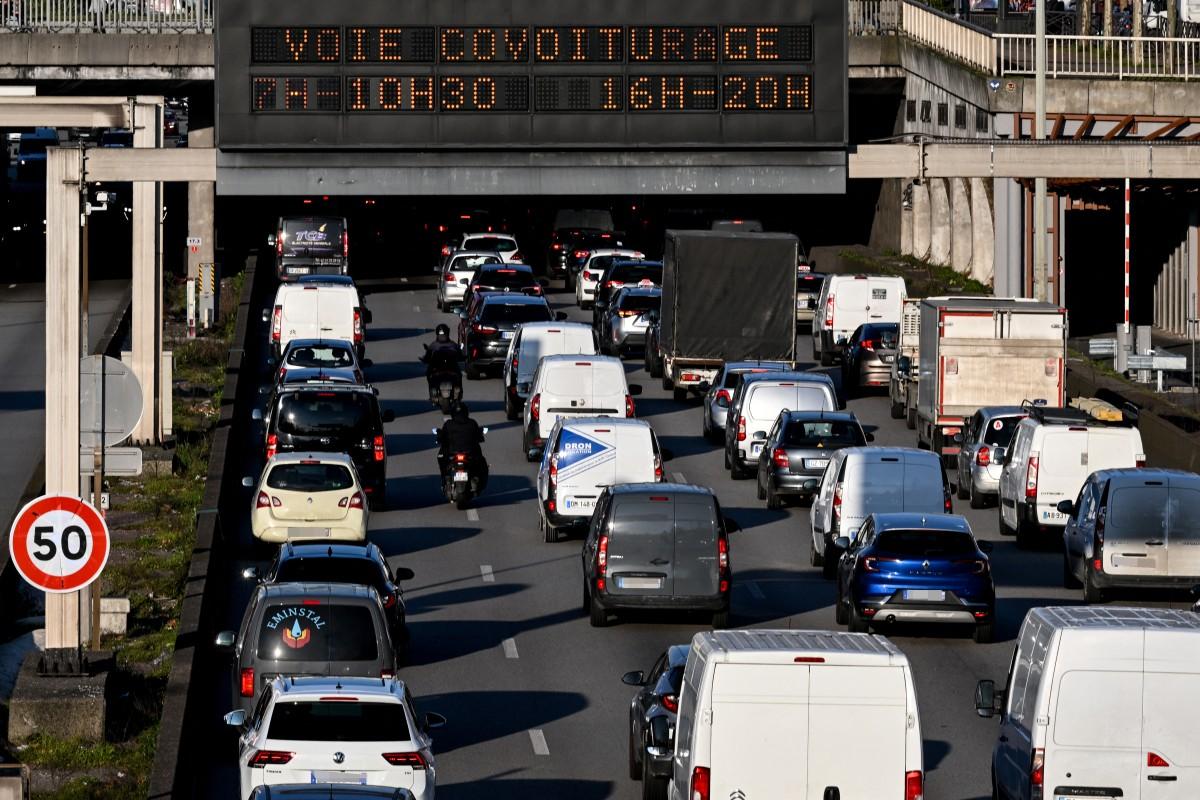 Cette photo prise à Paris le 3 mars 2025 montre des automobilistes conduisant leurs voitures devant un panneau de signalisation annonçant les heures d'ouverture de la nouvelle voie de covoiturage sur la rocade de Paris.