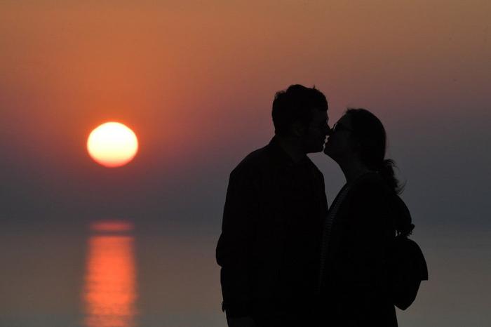Un couple s'embrasse devant le soleil couchant.
