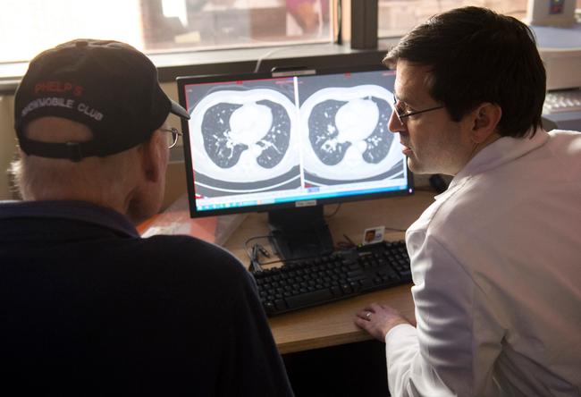 Le Dr Christian Hinrichs, chercheur à l'Institut national du cancer en immunothérapie pour les cancers HPV+, montre à un patient, survivant d'un cancer métastatique, la différence entre son scanner montrant des tumeurs cancéreuses et un scanner après traitement, après une journée d'examens médicaux ne montrant aucune récidive du cancer, à Bethesda, dans le Maryland.