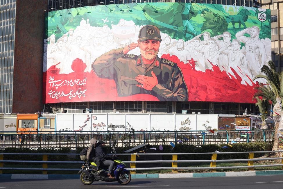Des Iraniens passent à moto devant une immense banderole à l'effigie de l'ancien commandant de la Force Qods du Corps des gardiens de la révolution islamique, Qassem Soleimani, le 31 décembre 2025, à l'approche du sixième anniversaire de son assassinat en Irak.