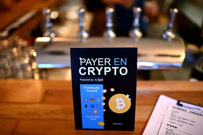 Cette photographie montre un panneau informant sur la possibilité de payer en cryptomonnaies via l'application mobile Lyzi à la microbrasserie et bar La Fracasse, à Talence, dans la banlieue bordelaise, le 26 juin 2025.