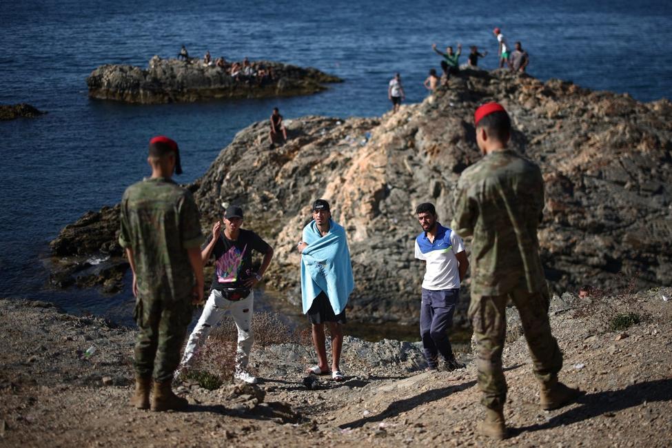 Des membres des forces d'infanterie « Regulares » de l'armée espagnole s'entretiennent avec un groupe de migrants près du poste-frontière de l'enclave espagnole de Ceuta, le 2 août 2026.